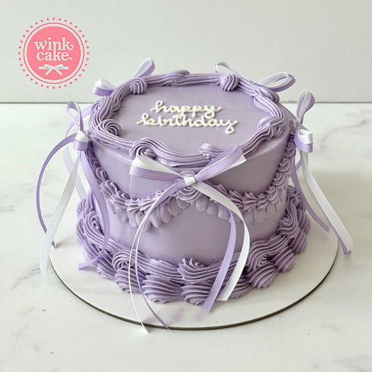 Một chiếc bánh sinh nhật kiểu công chúa màu tím được trang trí bằng ruy băng tím.